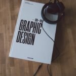 Discover graphic design history with this book and headphones on a wooden floor.